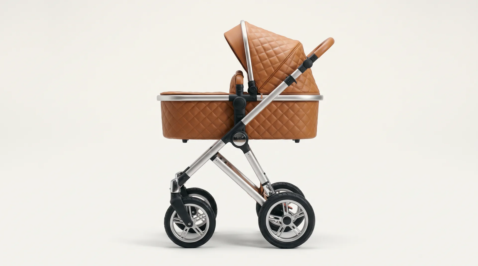 A high-landscape pram in profile: quilted tan leather bassinet on a brushed aluminium frame.